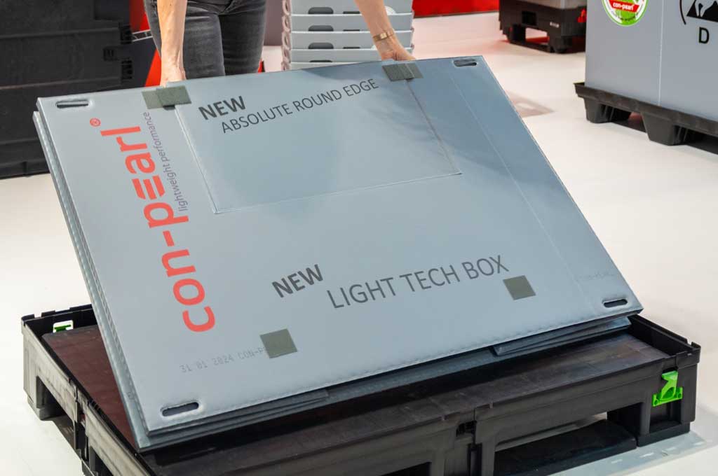 Mitarbeiterin hebt gefalteten Container von Boden auf