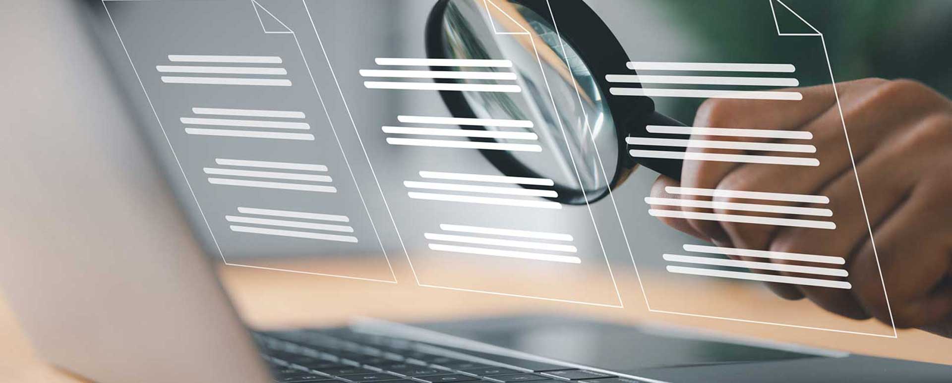 Hand mit Lupe vor drei Dokumentenicons und aufgeklapptem Laptop